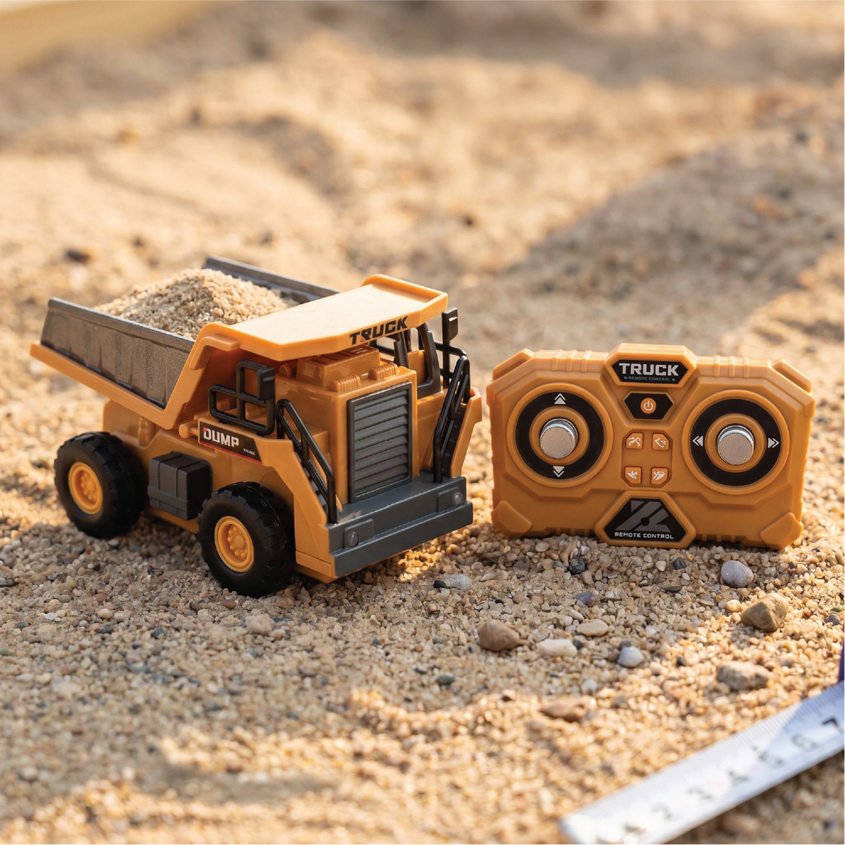 L.O.T Cars Rumble 1:64 RC dump truck loaded with sand, parked on sand next to its two-dial remote control