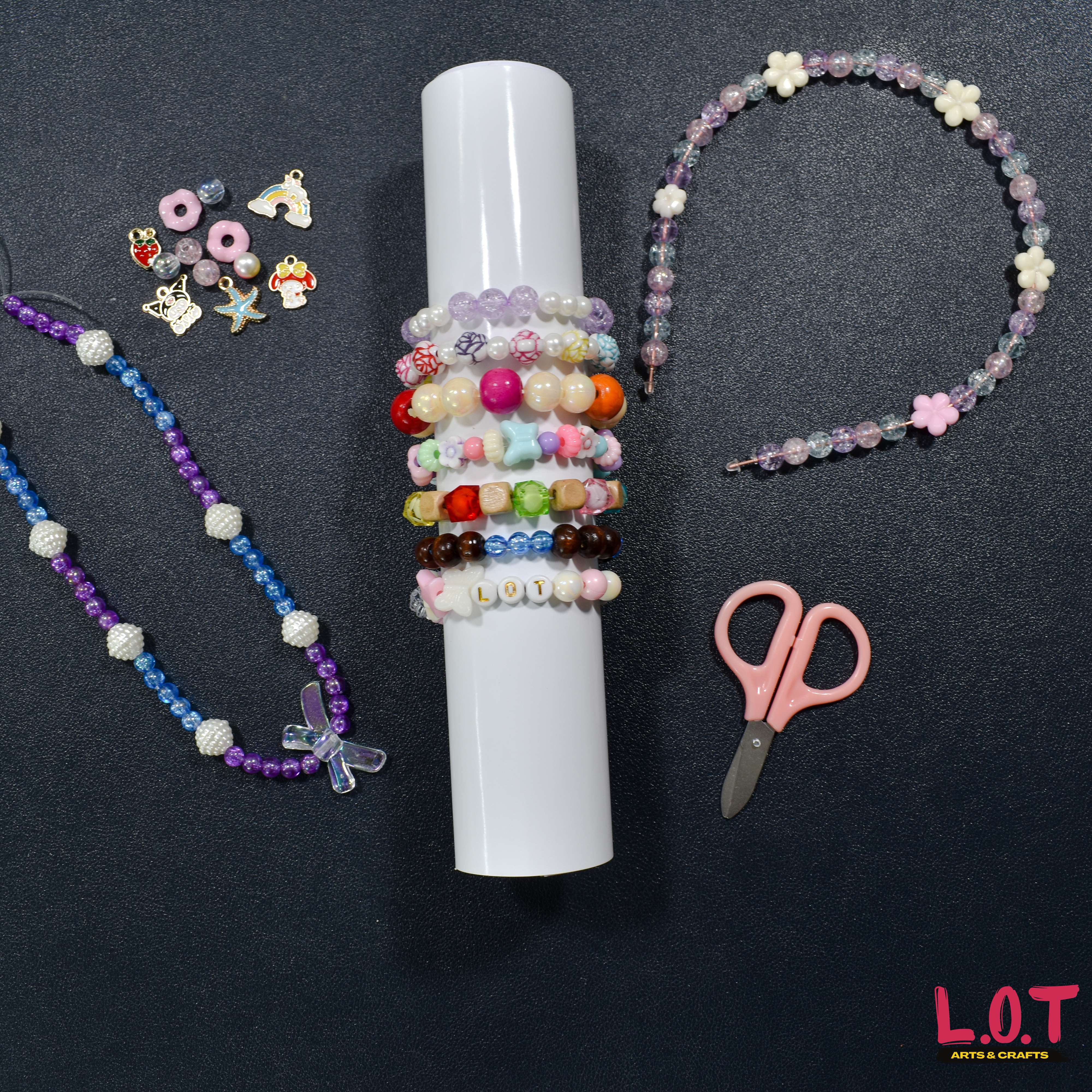Beaded necklaces, bracelets, and a pair of scissors on a dark surface with 'L.O.T' branding.